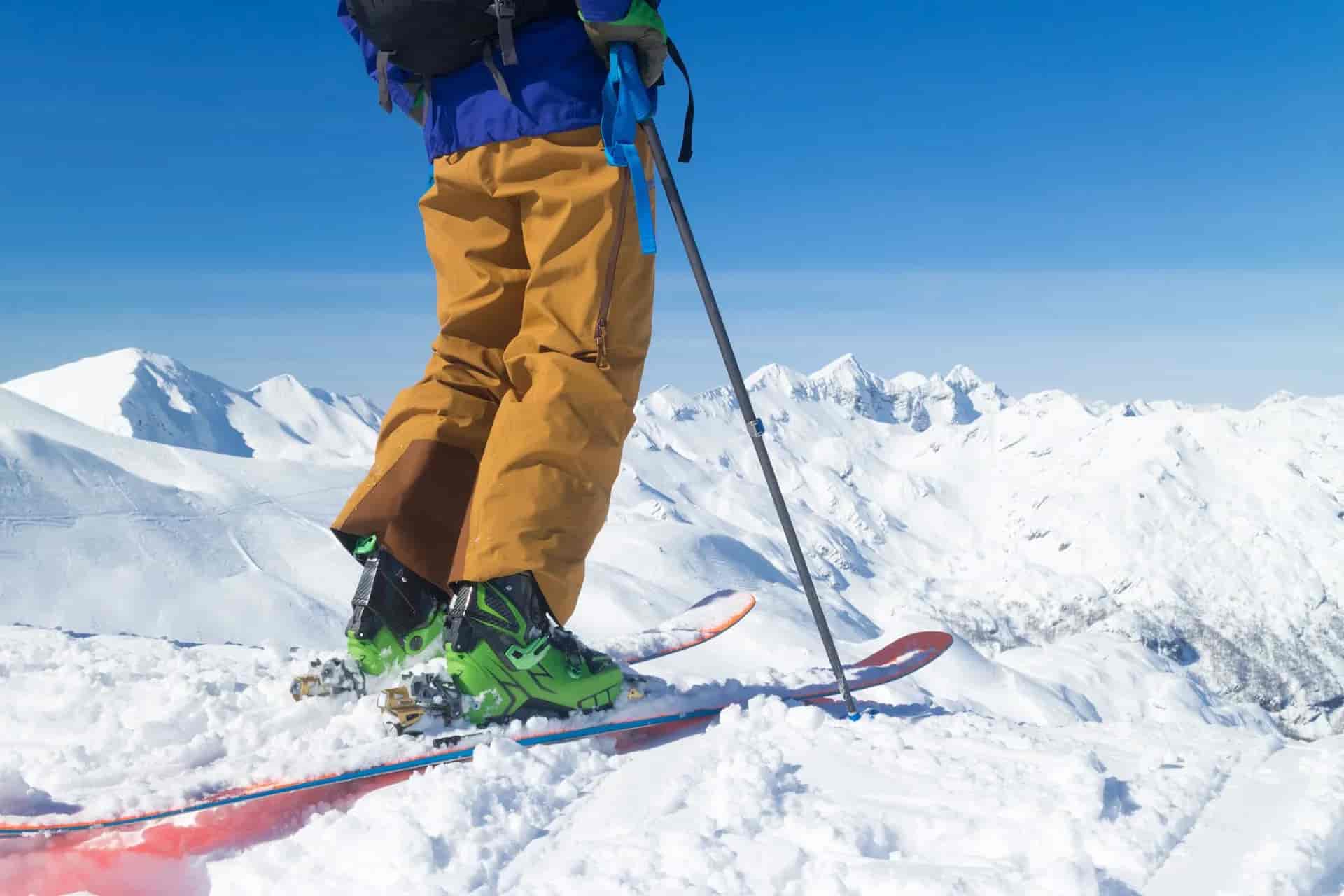 Skier with skis and poles standing on snowy mountain peak under clear blue sky