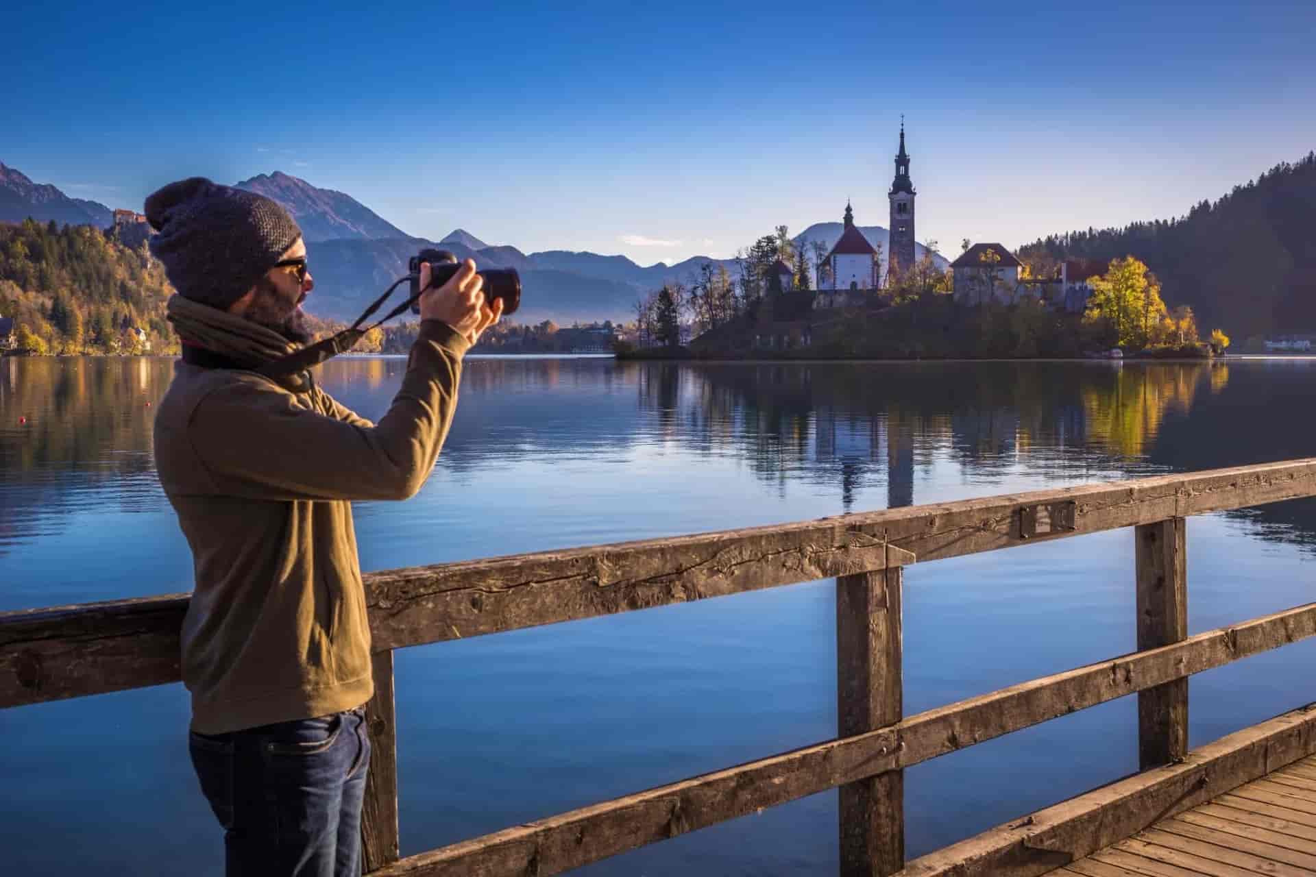 Photographer capturing Lake Bled island church with mountains in autumn light