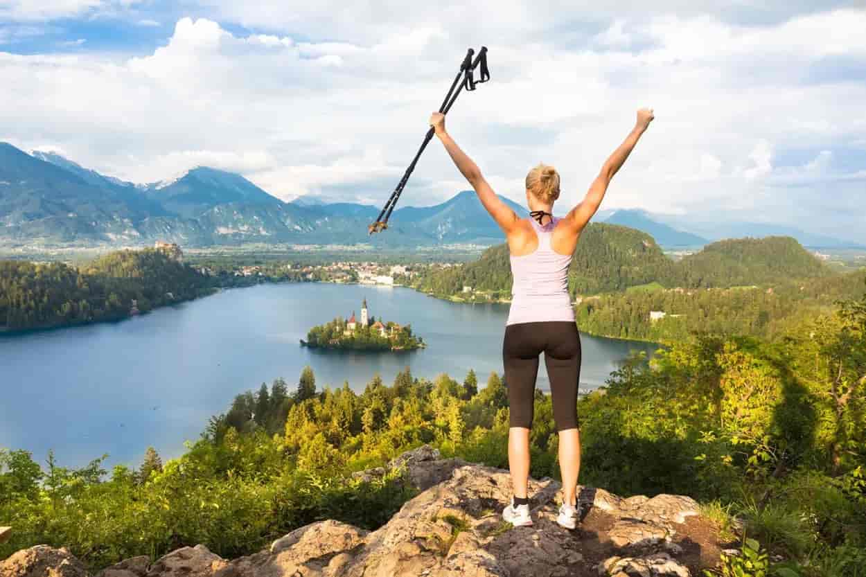 Hiker celebrating on viewpoint overlooking Lake Bled island and Julian Alps in Slovenia