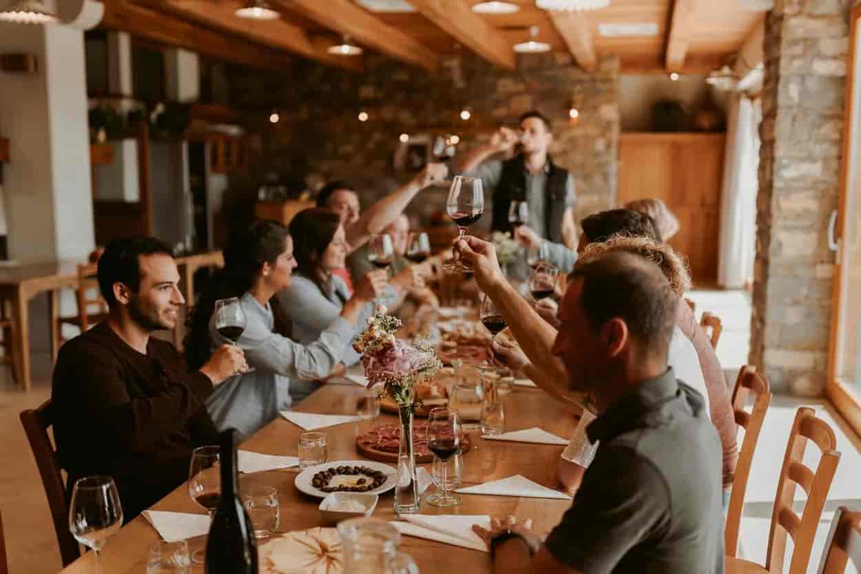 Group toasting with red wine glasses during a tasting lunch in a rustic stone and wood interior.