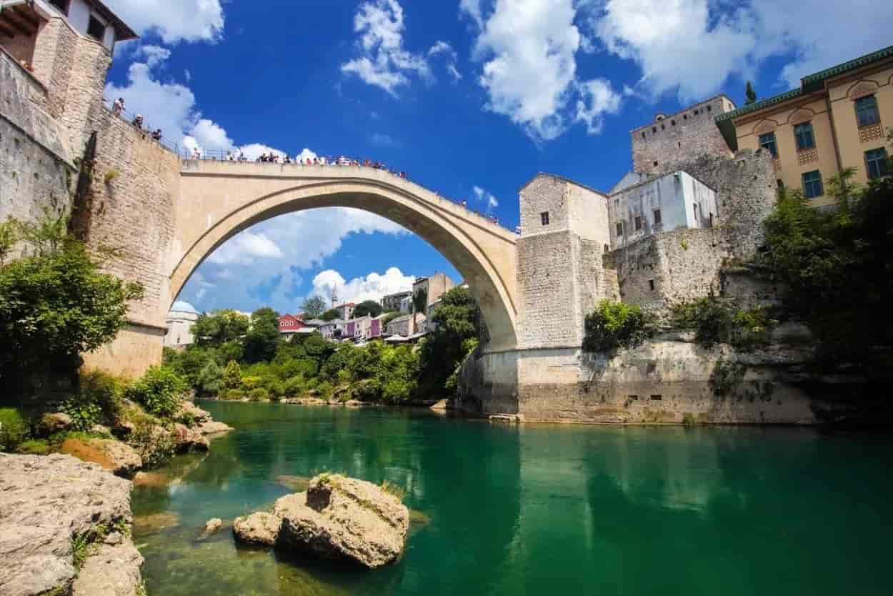 Stari Most bridge over emerald river with stone buildings and blue sky in Mostar.