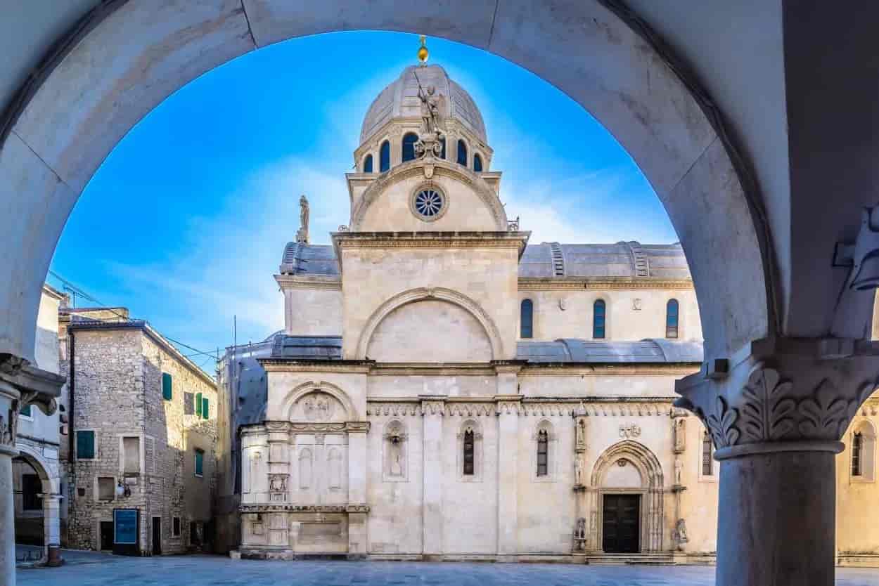 St. James Cathedral facade framed by an archway in Šibenik, Croatia, under a blue sky.