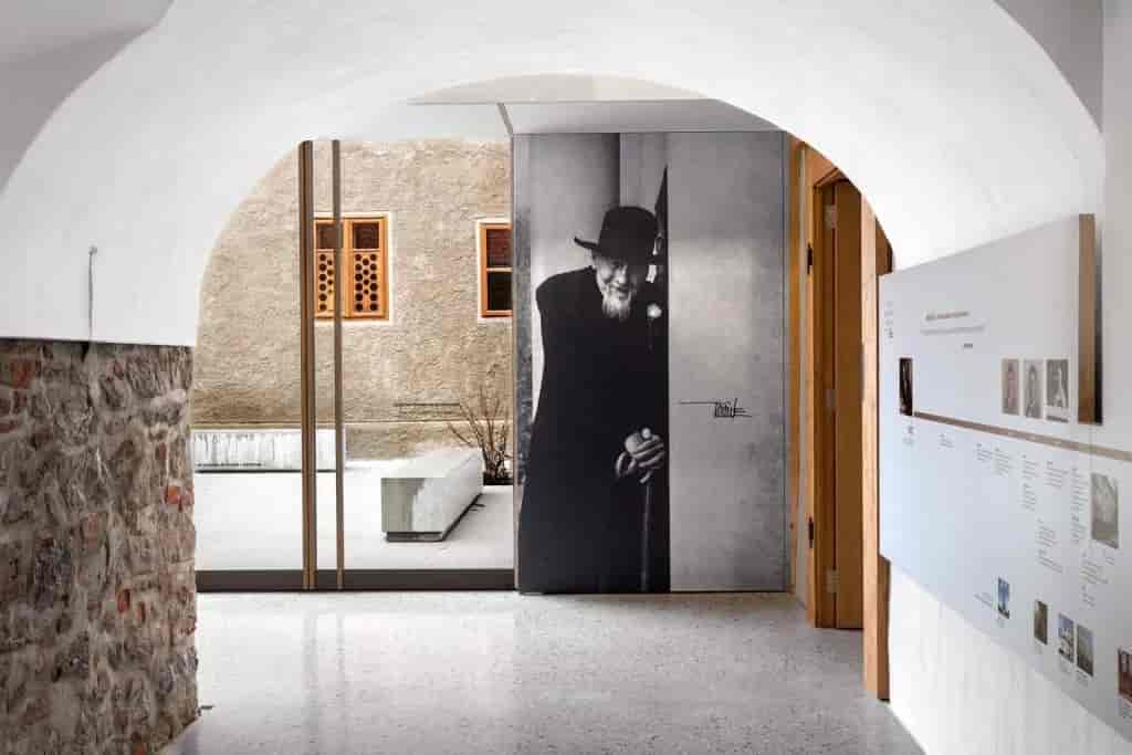 Interior view of Plečnik House entrance with stone wall, timeline display, and portrait of a man.