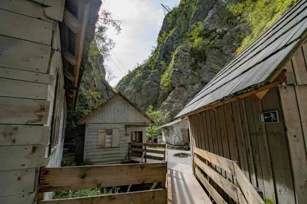 Wooden cabins nestled between steep, green, rocky cliffs with wooden walkways.
