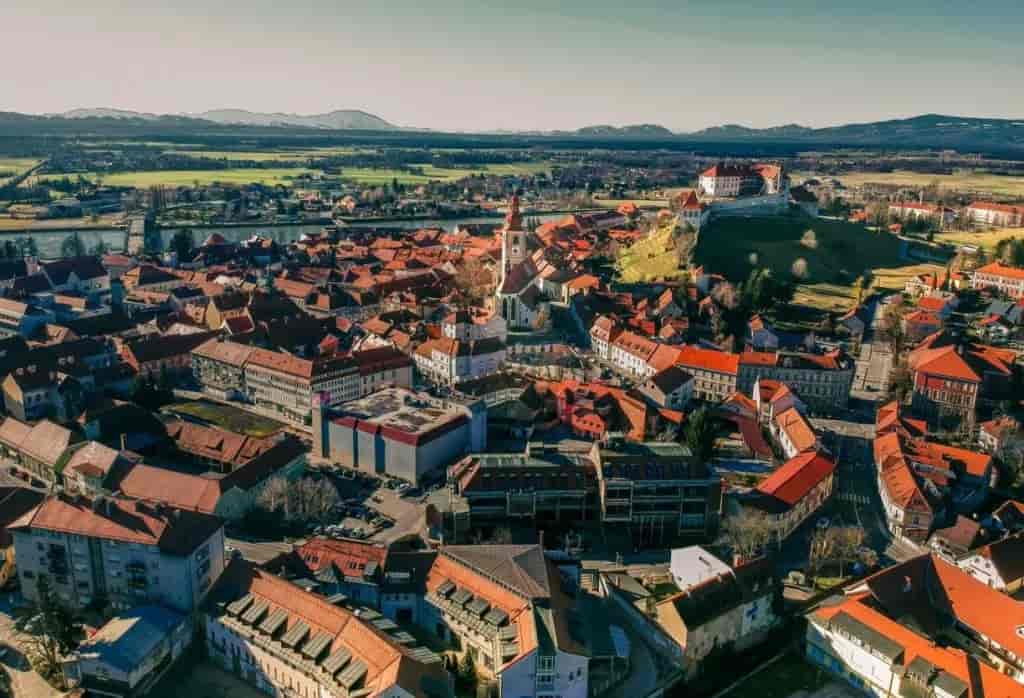 Aerial view of Ptuj Old Town with red roofs, a church tower, and a castle on a hill.