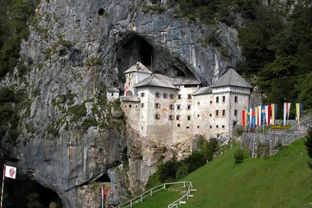 Predjama Castle built into a cliff face with flags displayed on the green hillside.