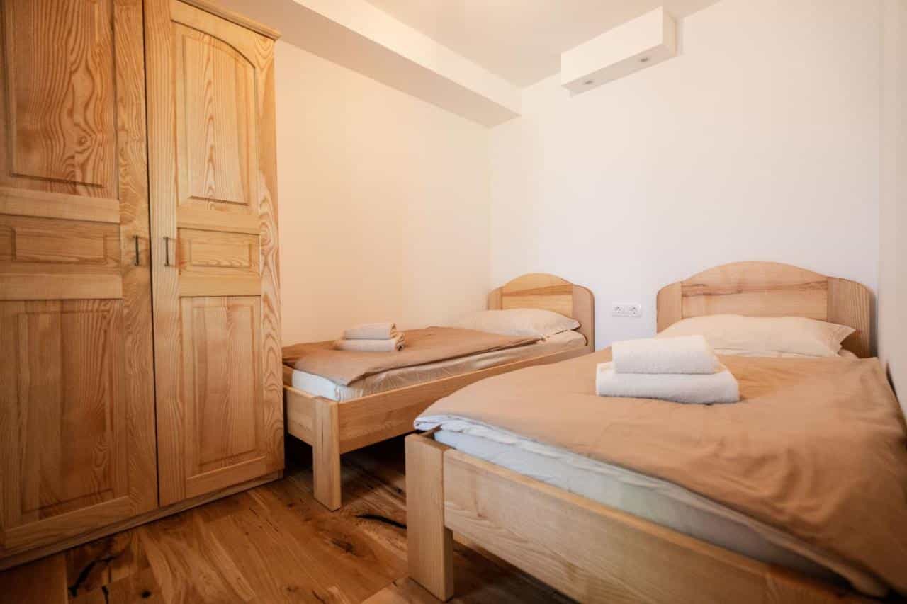 Twin beds with wooden frames and white towels in a bright room with a large wooden wardrobe.