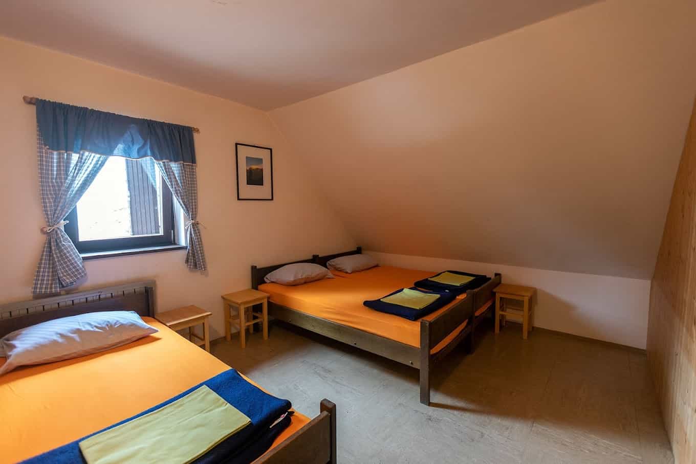 Attic bedroom with orange sheets, wooden beds, and plaid curtains at Erjavčeva koča.