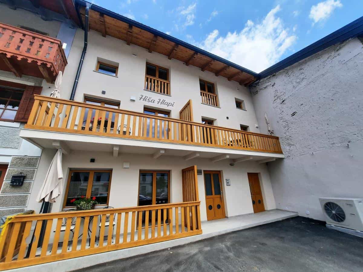 Apartments Hiša Hlapi building with wooden balconies under a blue sky with clouds