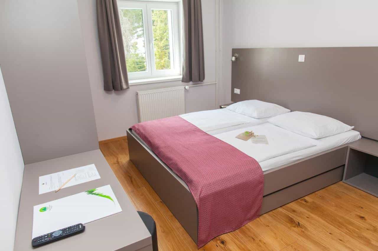 Twin beds with white linens and pink throw in Hotel Pokljuka room with wooden floor.