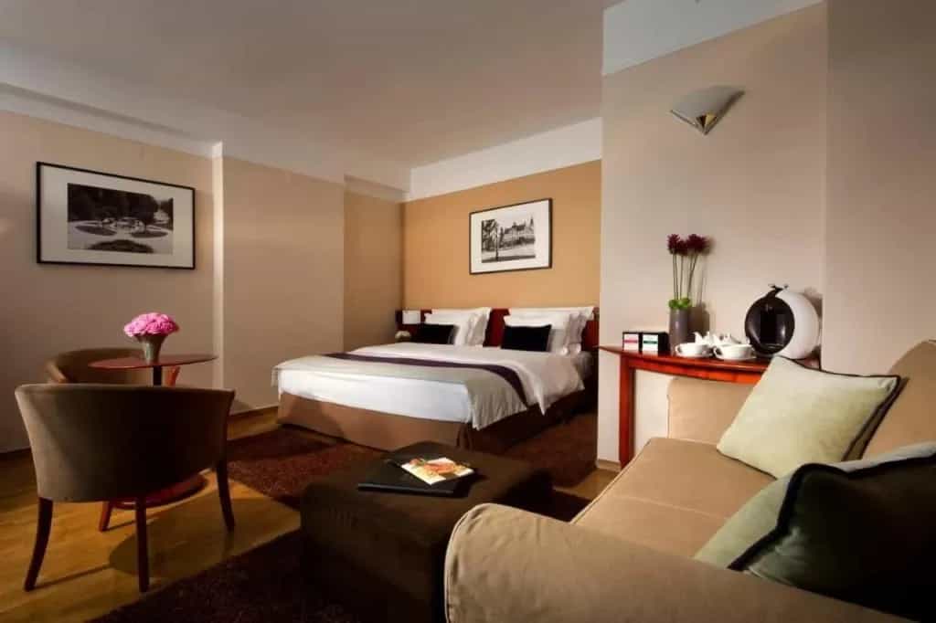 Hotel Slon room with queen bed, seating area, and coffee maker in warm tones.