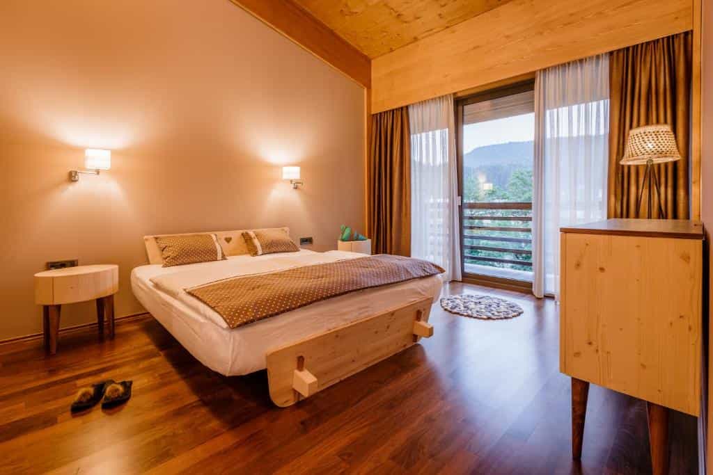 Hotel bedroom with wooden accents, polka dot bedding, and balcony view of mountains.