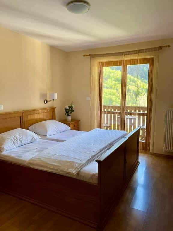 Hotel bedroom with wooden bed, white linens, and balcony view of green mountains.
