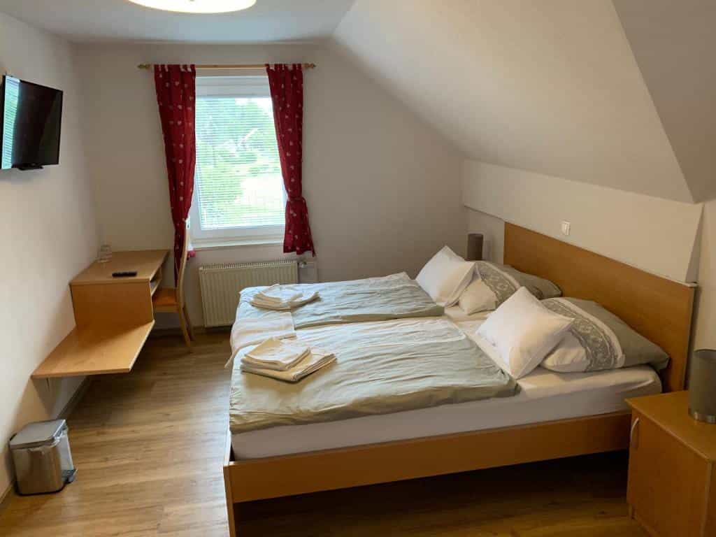 Guesthouse bedroom with twin beds, wooden furniture, and window with red curtains