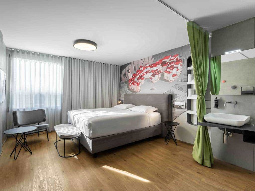 Modern hotel room with wood floor, white bedding, and colorful mural art near sink area