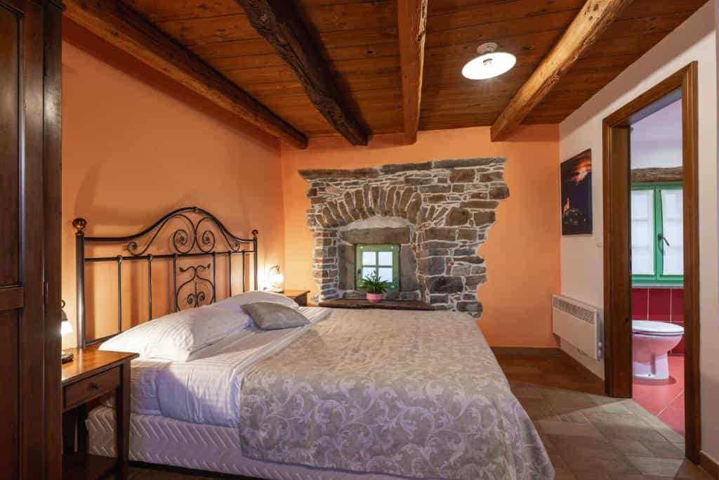 Bedroom with iron headboard, stone alcove window, and exposed wooden ceiling beams.