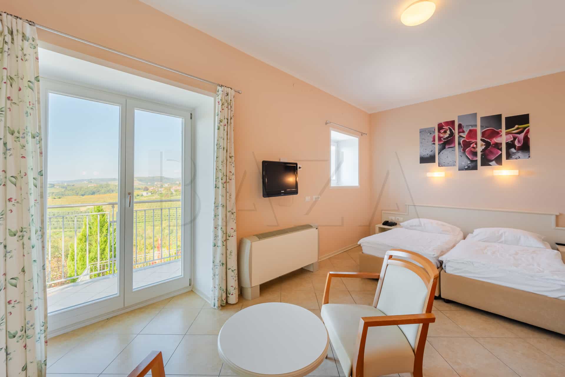 Hotel room with twin beds, balcony view of rolling green hills, and orchid artwork.