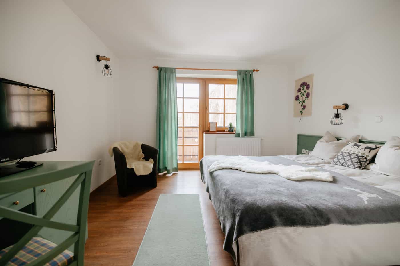 Hotel bedroom with a double bed, green curtains, armchair, and wooden furniture.