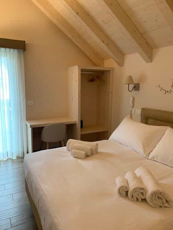 Hotel room with double bed, wooden ceiling beams, desk, and open wardrobe.