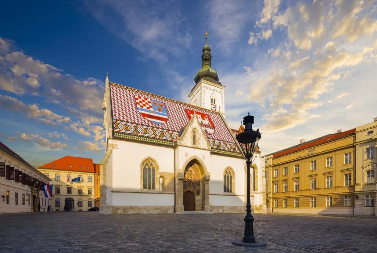 Church of St. Mark in Zagreb with colorful tiled roof and stone square at sunset.
