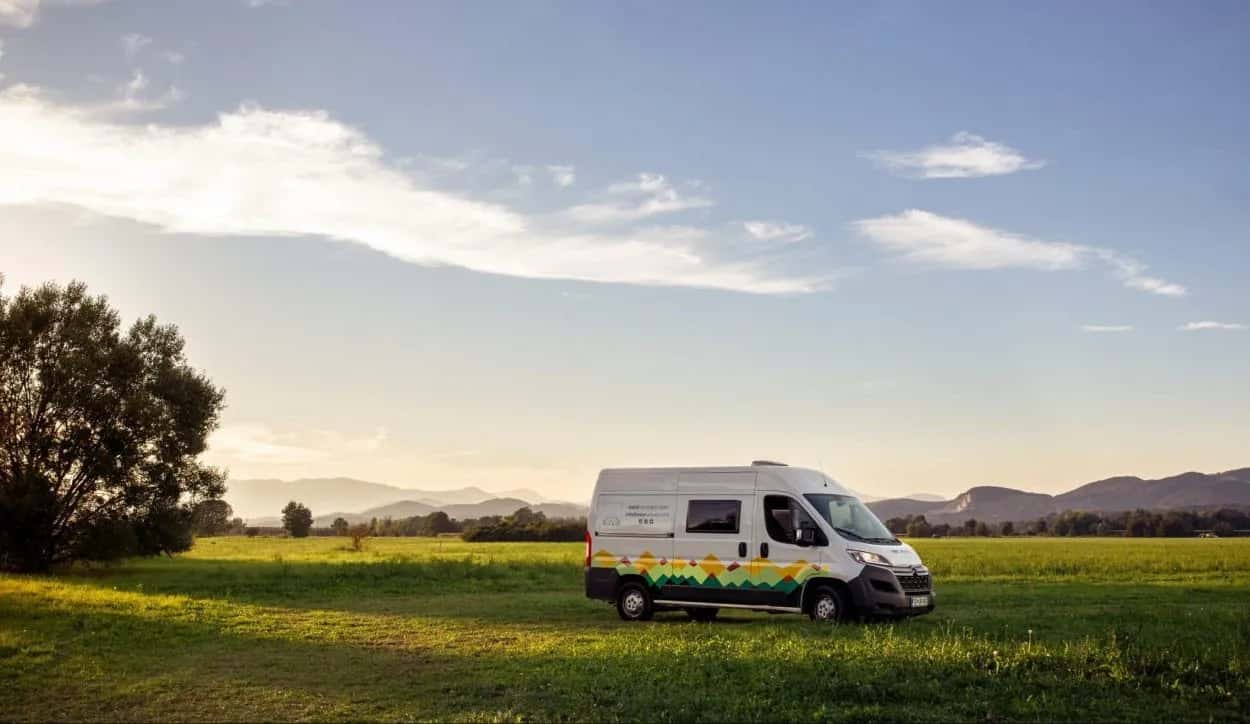Camper van parked in a grassy field with rolling hills and mountains in the background