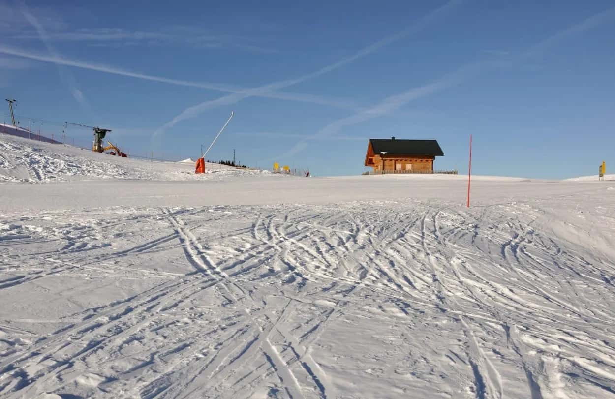 Ski slope with many tracks leading toward a wooden cabin under a clear blue sky at Dreilandereck-Arnoldstein.