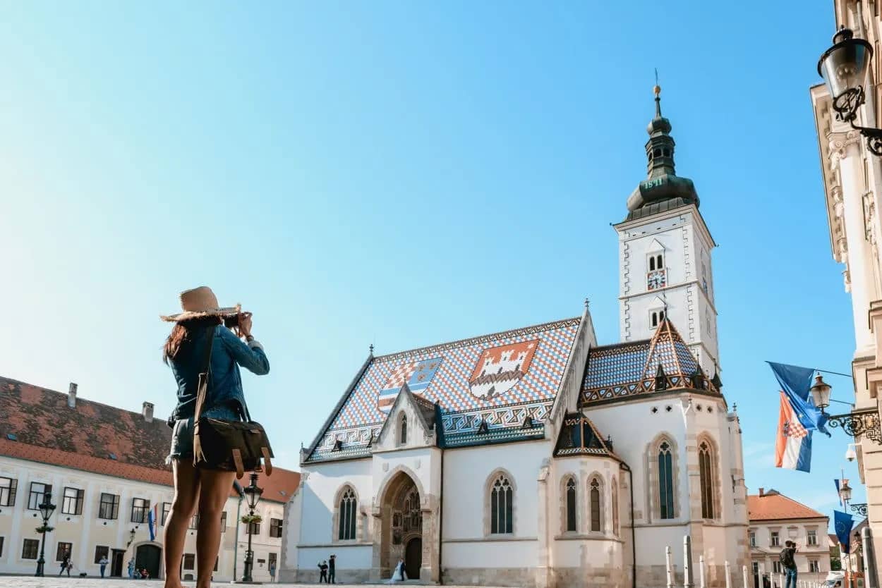 Tourist photographing St. Mark's Church with colorful tiled roof in Zagreb old town.