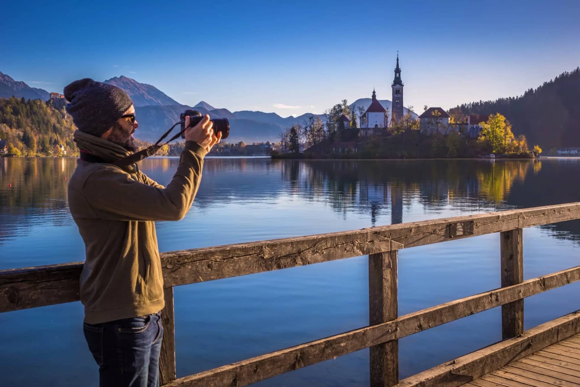 Photographer capturing Lake Bled island church with mountains in autumn light