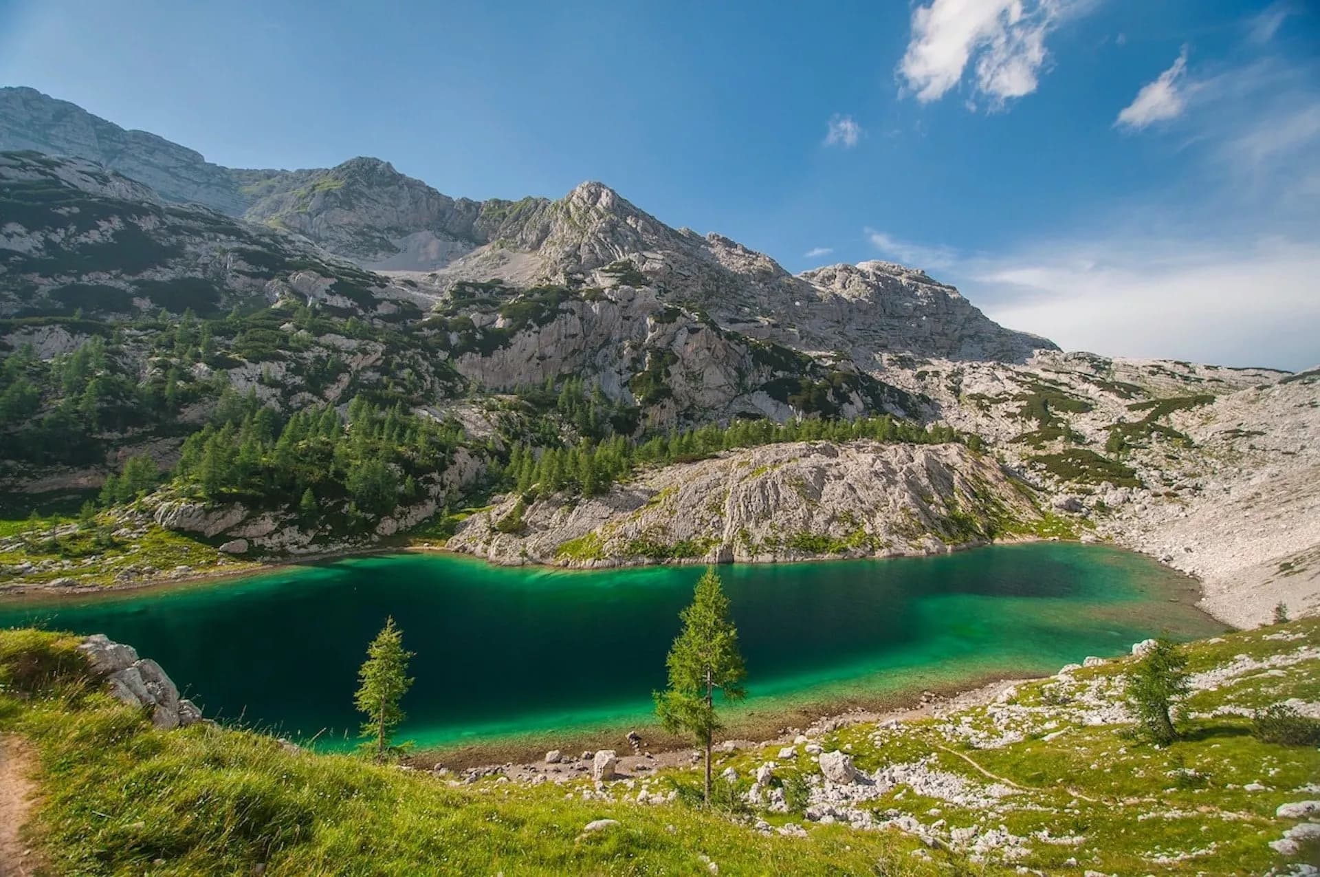 Emerald mountain lake surrounded by rocky slopes and green pine trees under a blue sky.