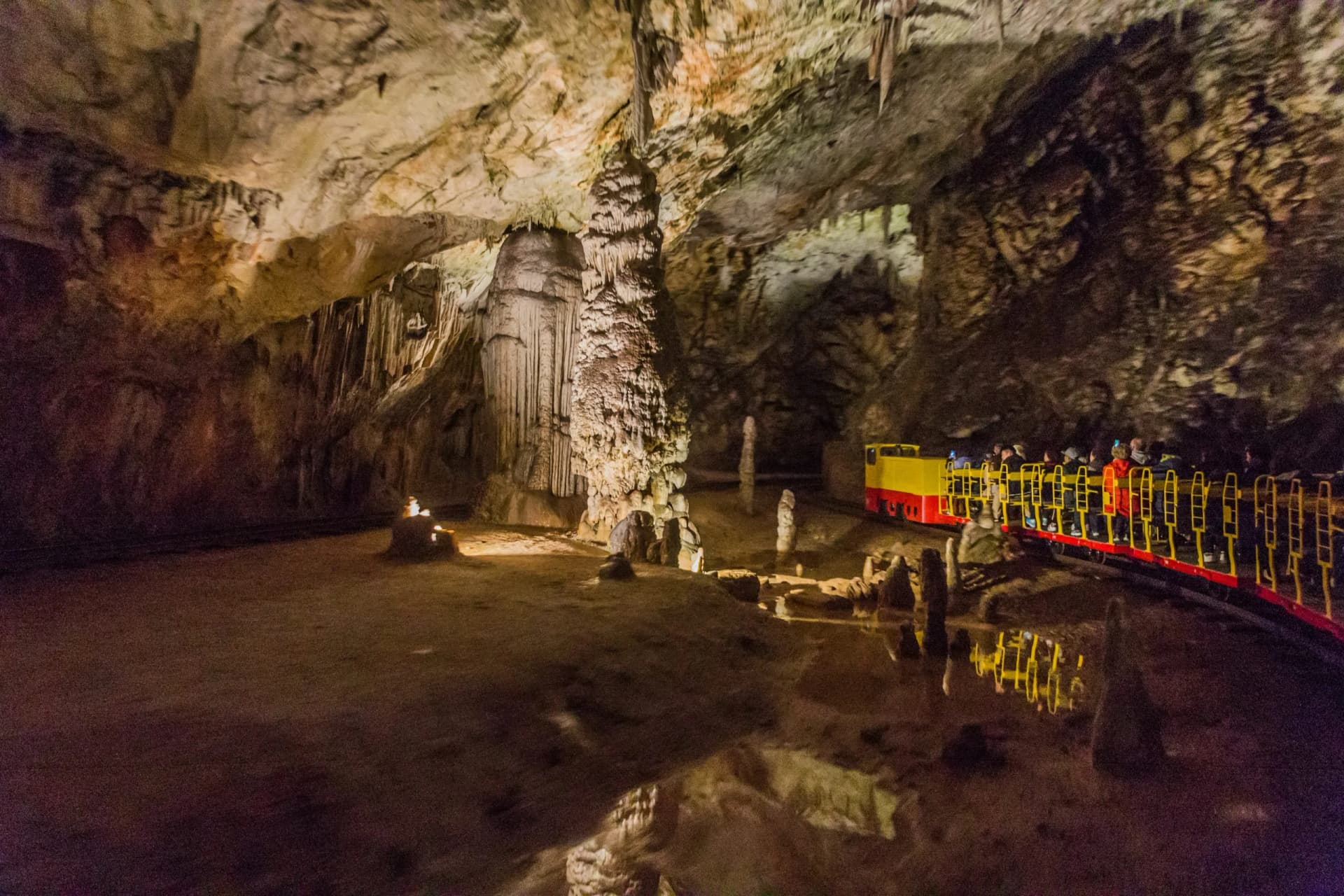 Tourist train moving through a large cave chamber with illuminated stalactites and stalagmites in Postojna Cave.