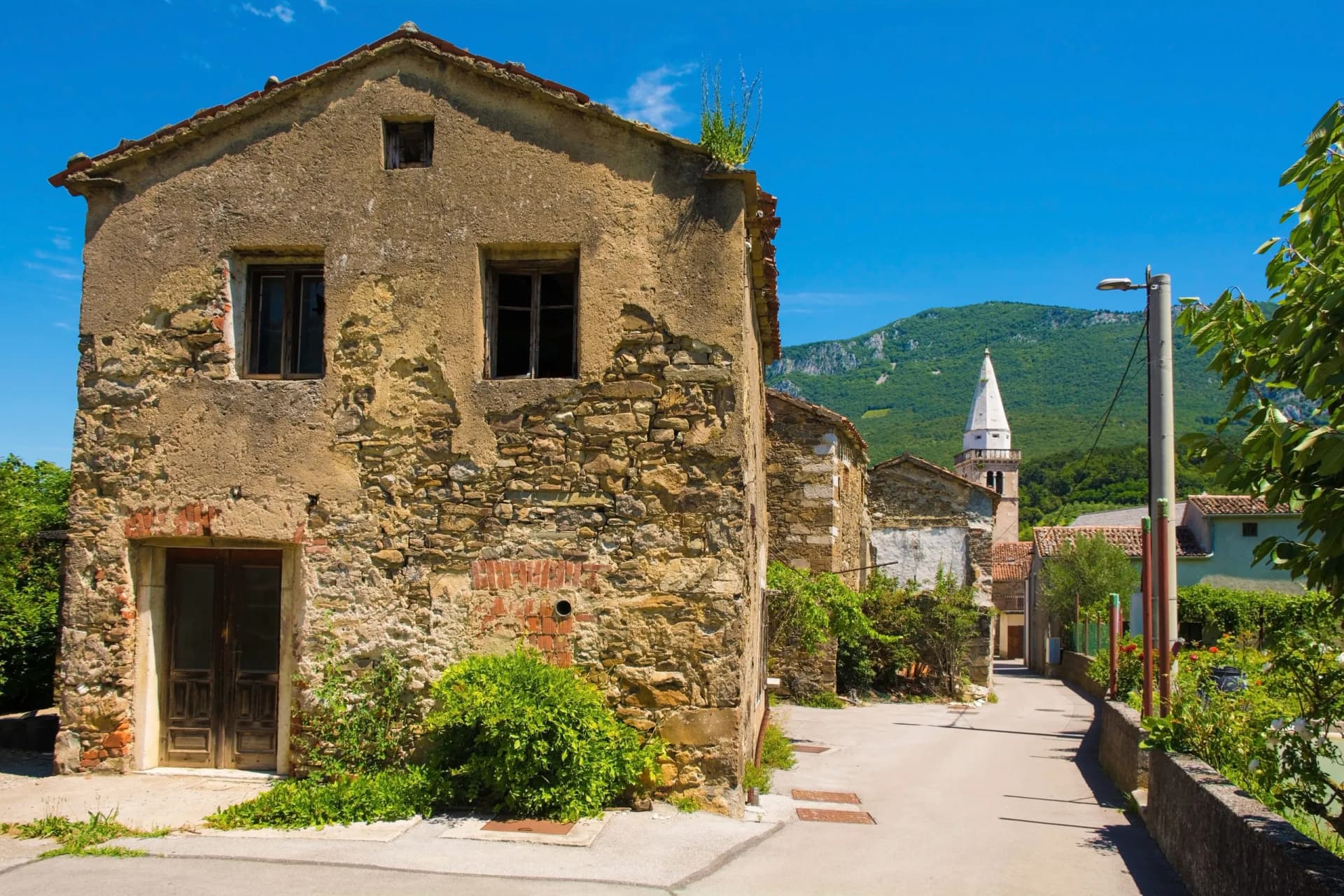 Historic stone building on street leading toward church spire and green mountain in Podnanos.