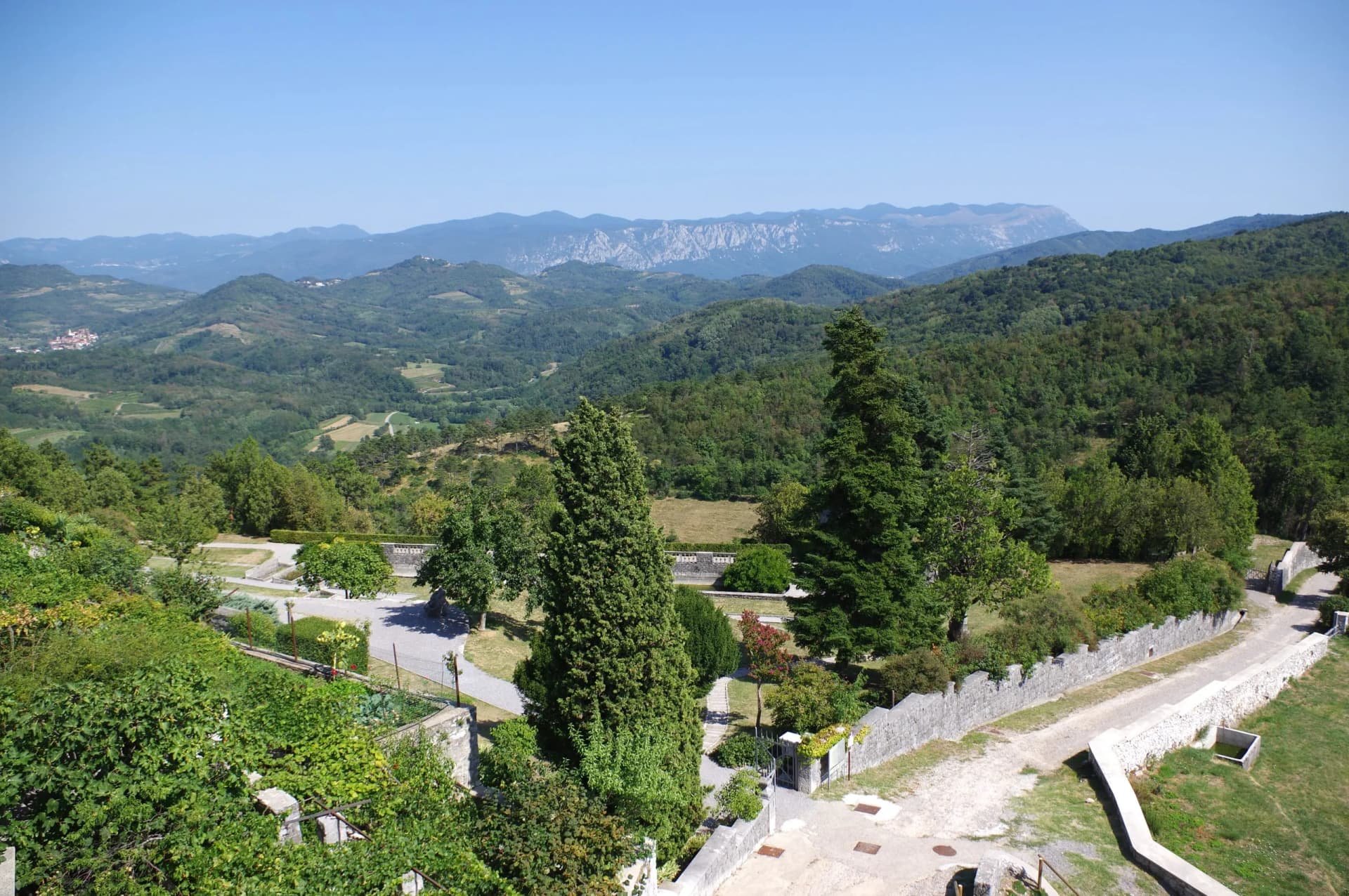 View from Stanjel featuring lush green hills, distant mountains, and a stone-walled garden area.