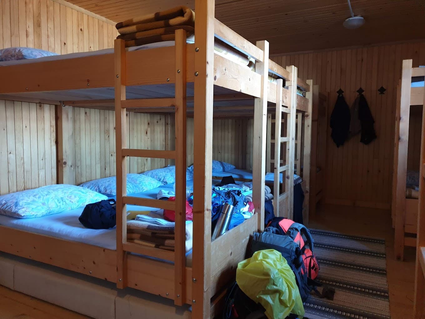 Wooden bunk beds in a rustic cabin dormitory with luggage on the floor.