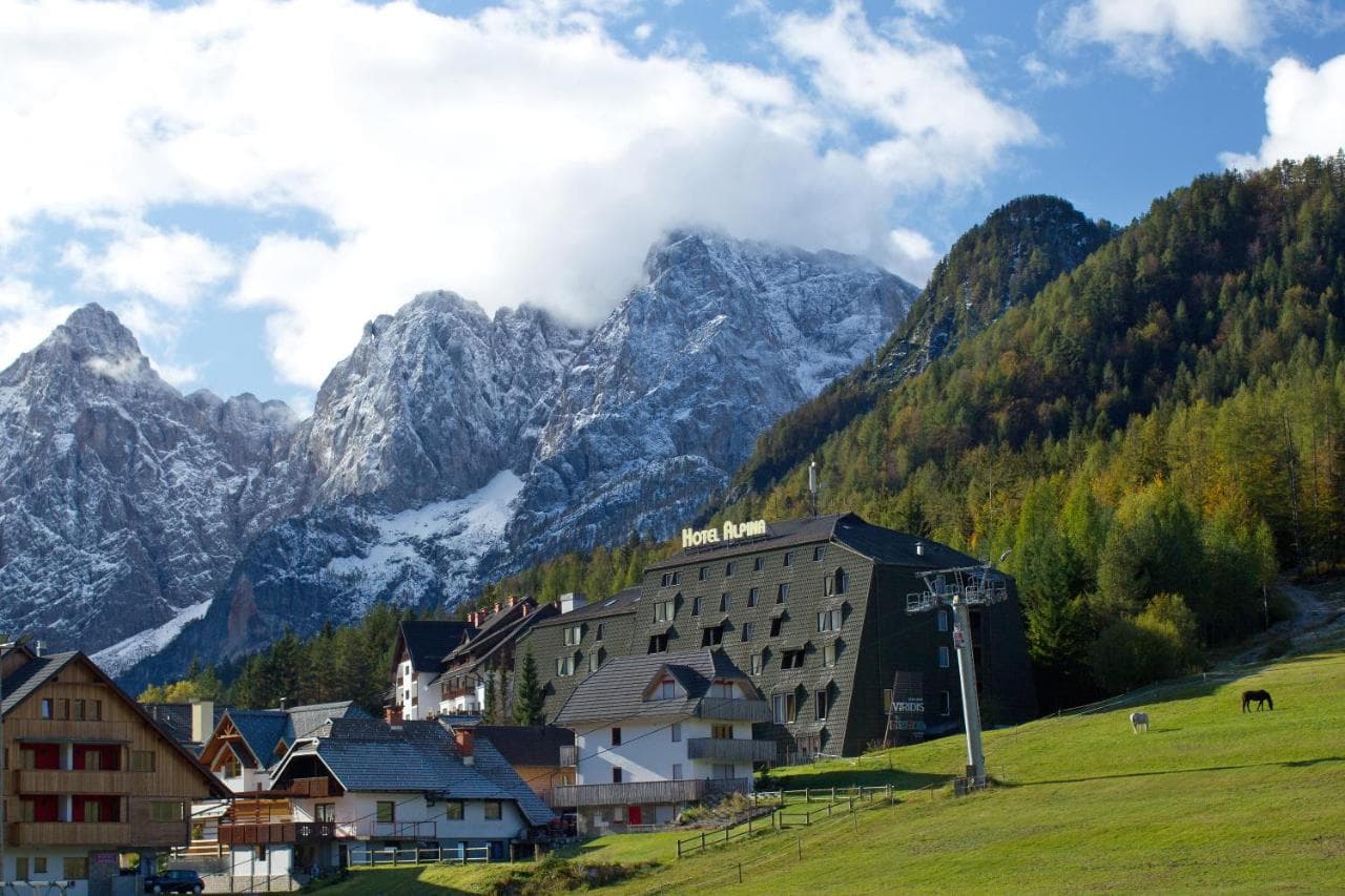 Hotel Alpina in alpine village below snow-dusted mountains with green hillside