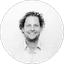 Black and white portrait of a smiling man with curly hair in a collared shirt.
