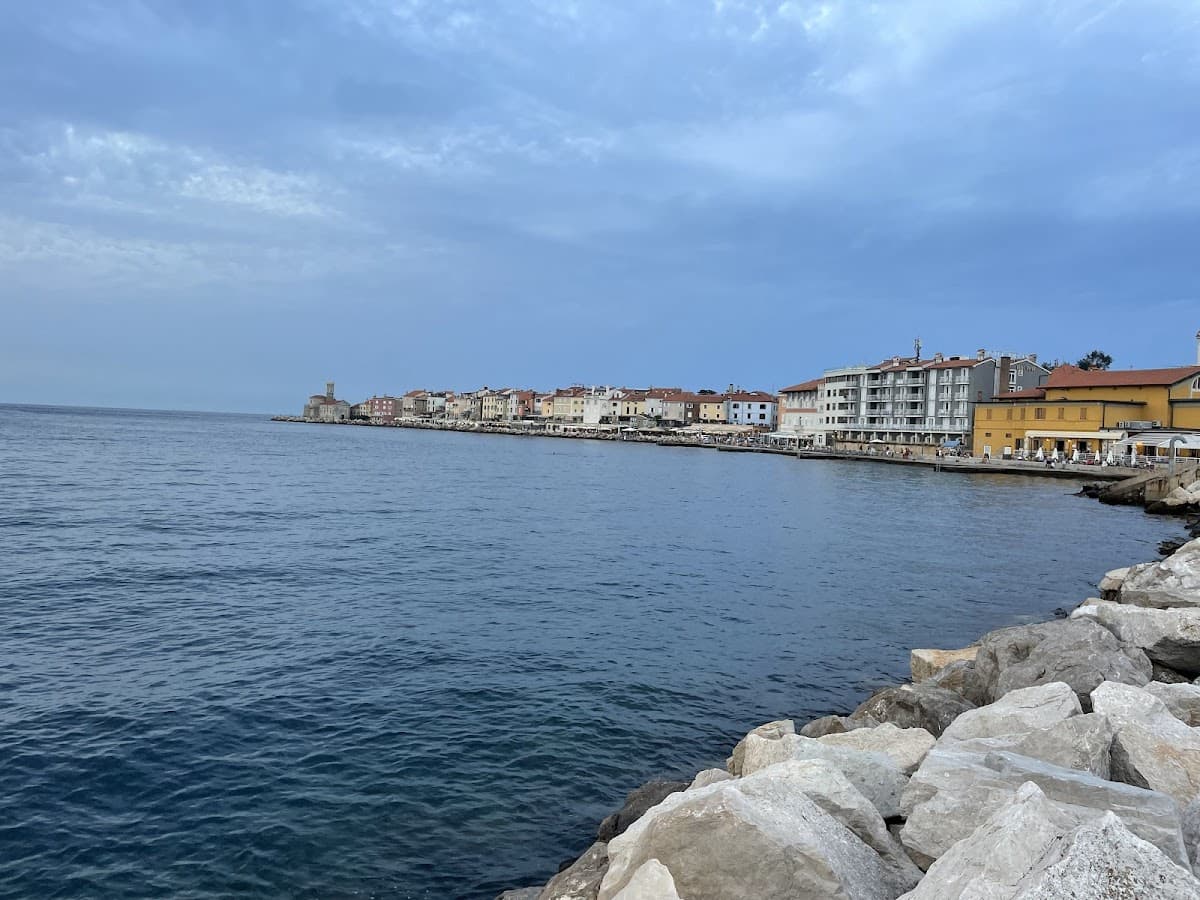 Coastal town waterfront with colorful buildings and a prominent church tower viewed over dark blue sea water.