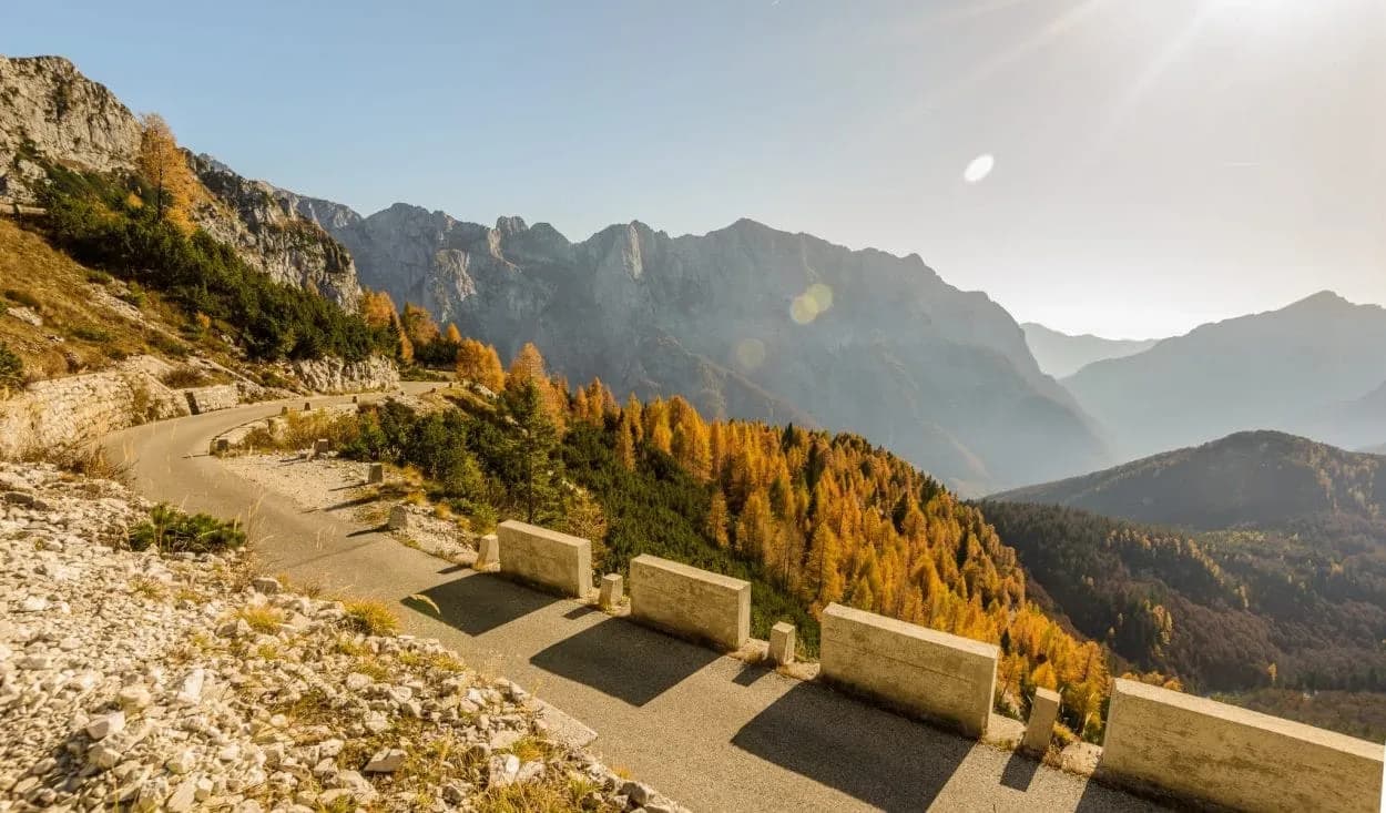 Winding mountain road with autumn foliage and layered peaks under bright sun