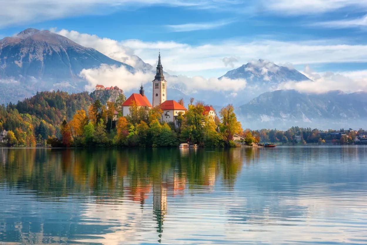 Church on Bled Island reflected in the lake with mountains and autumn foliage