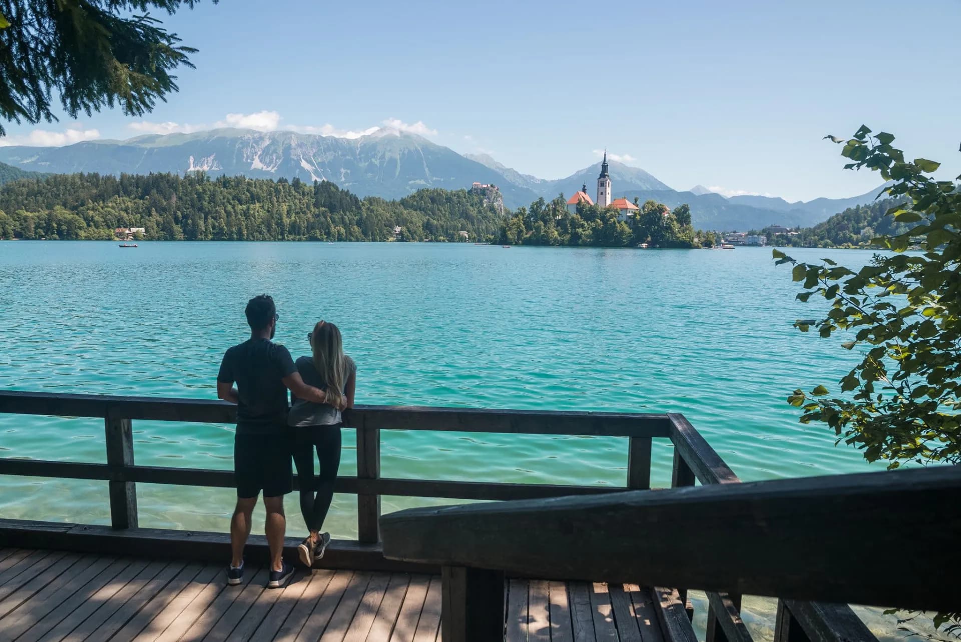 Couple on boardwalk overlooking Lake Bled island church and Julian Alps mountains
