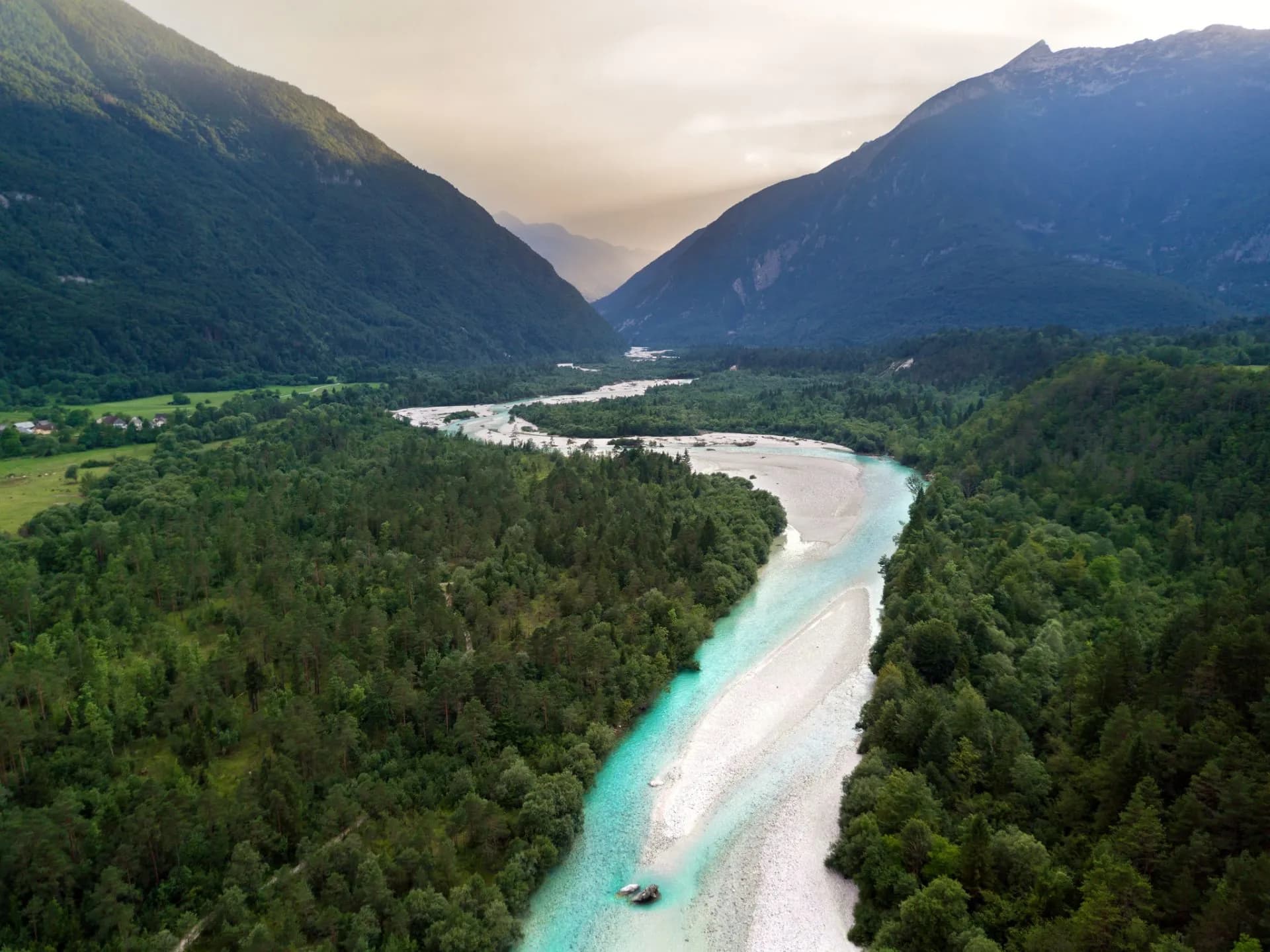 Turquoise river winding through a valley with dense green forests and steep mountainsides.