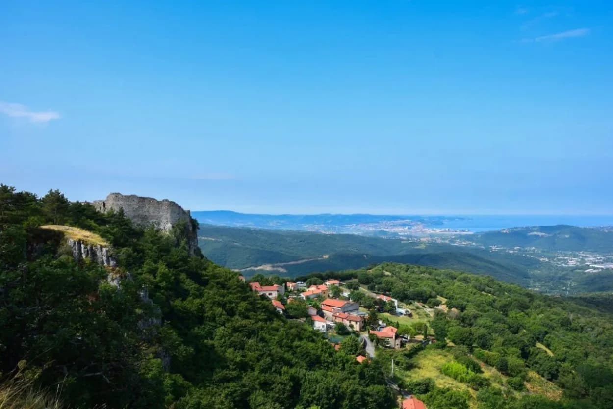 View from Socerb featuring castle ruins, village, and distant sea under a clear blue sky.