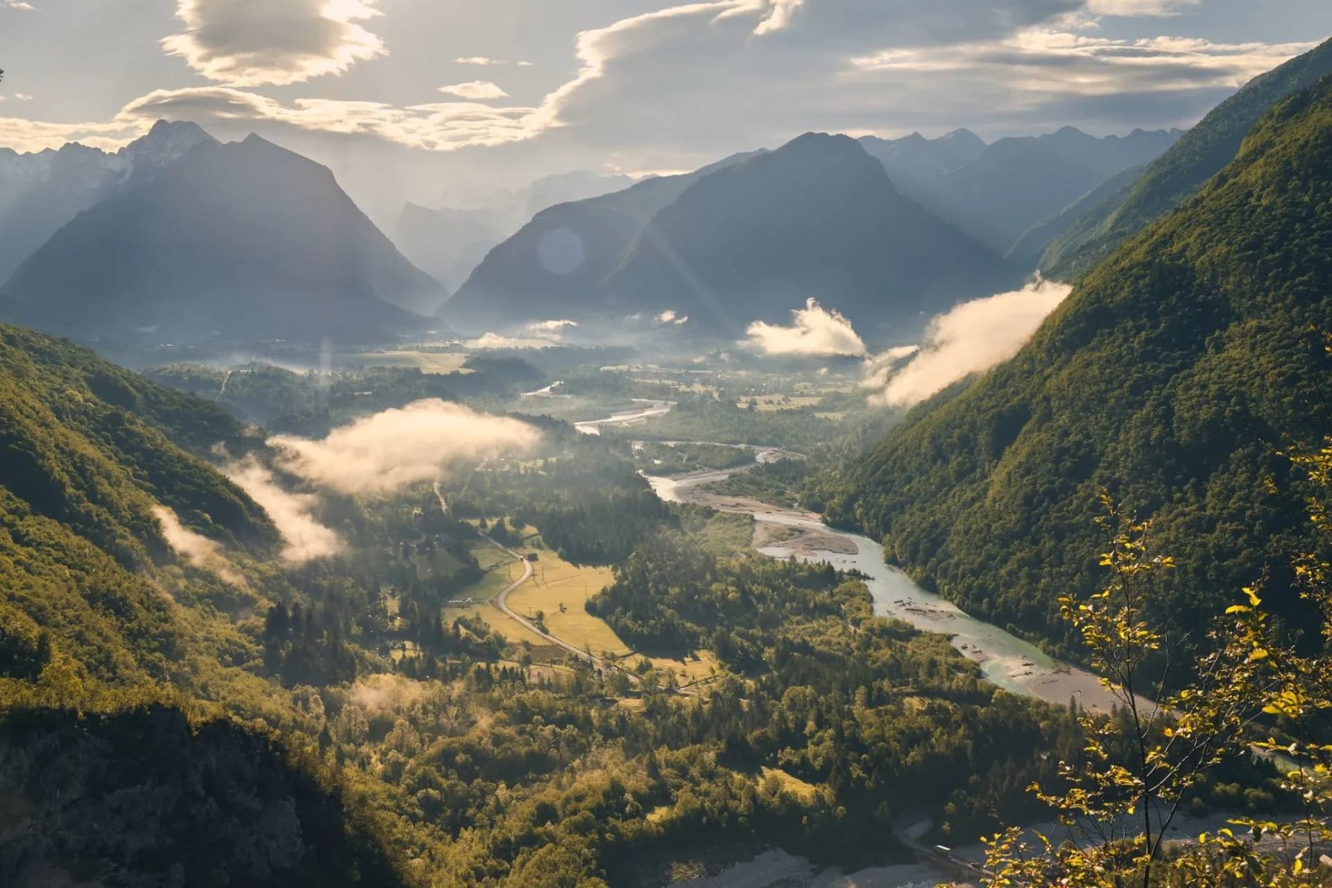 Misty Soca Valley with winding river, lush green mountains, and sunlit clouds near Bovec.
