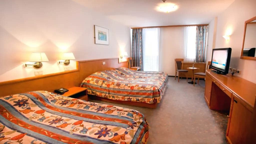 Hotel room with two beds, floral bedding, wooden furniture, and a television in Hotel Cerkno.