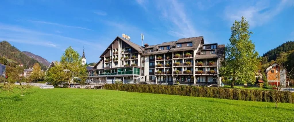 Hotel Cerkno building with balconies in a green valley under a blue sky