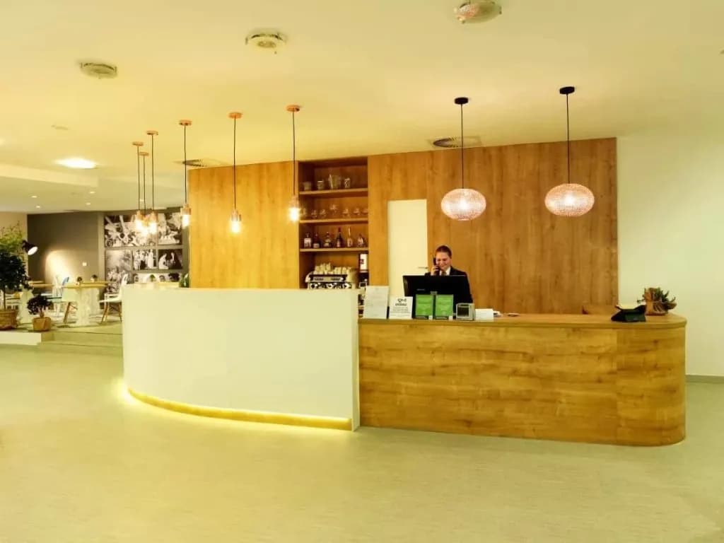 Hotel reception desk with wood paneling, modern lighting, and staff member on the phone.
