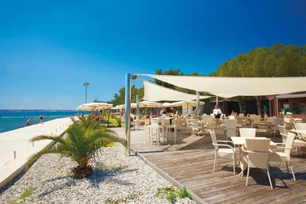 Outdoor cafe with white seating under awnings next to a concrete sea wall at Hotel Mirna beach.