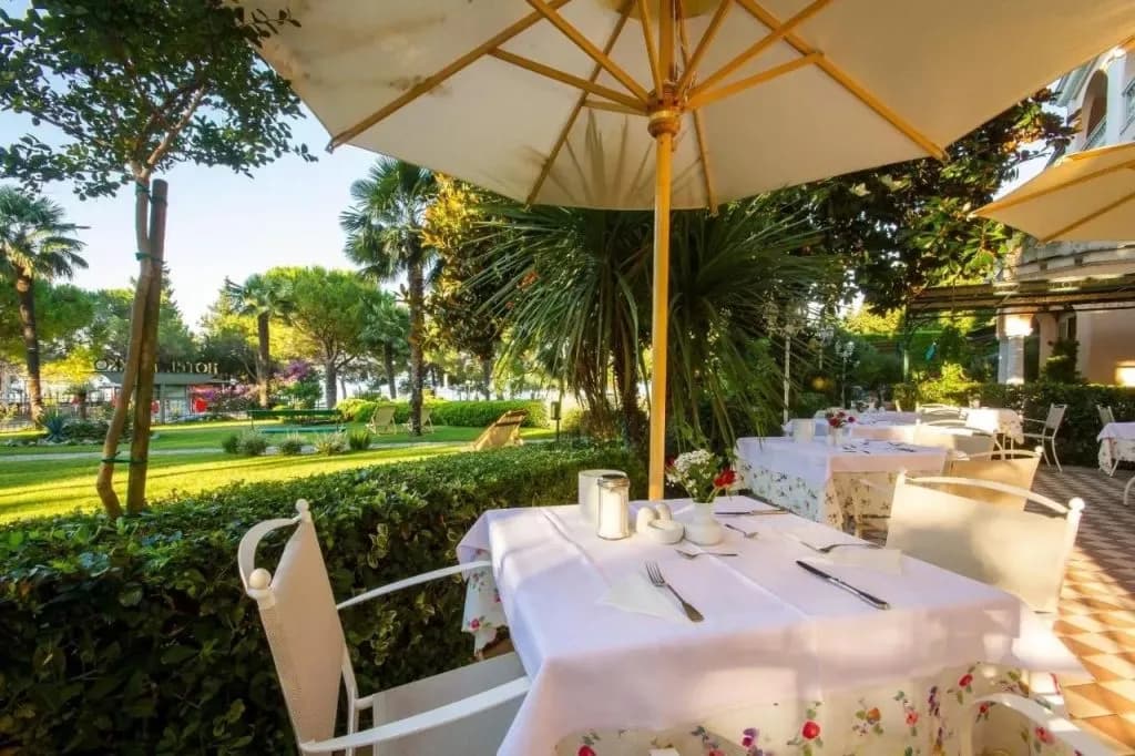 Outdoor dining terrace at Hotel Marko with white tables, umbrellas, and lush garden view.