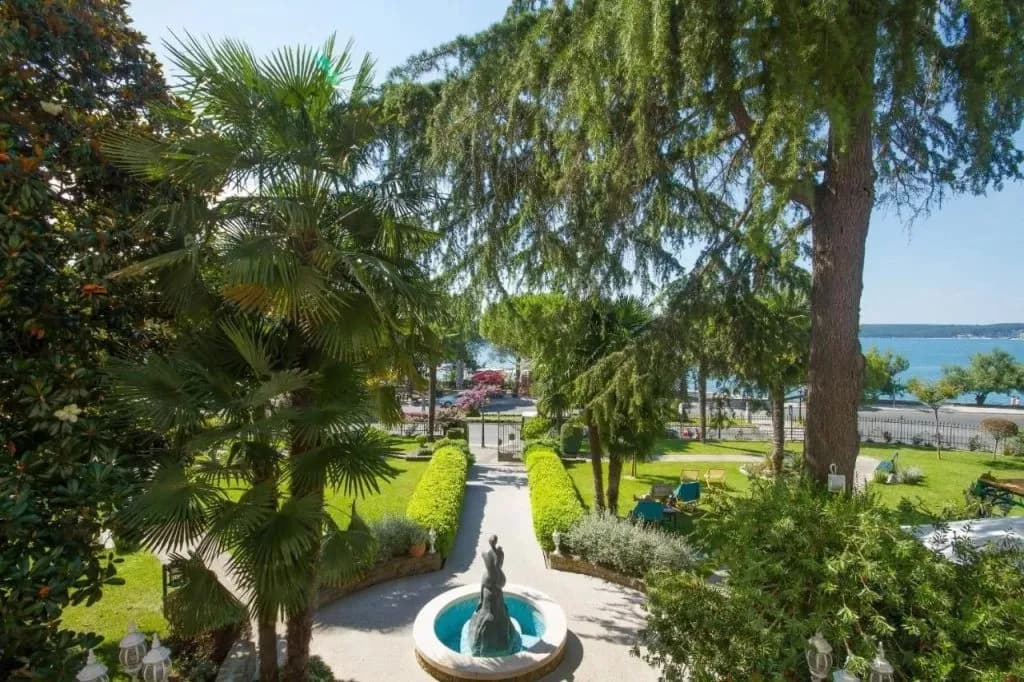 Lush garden with palm trees, fountain statue, and sea view near Hotel Marko.