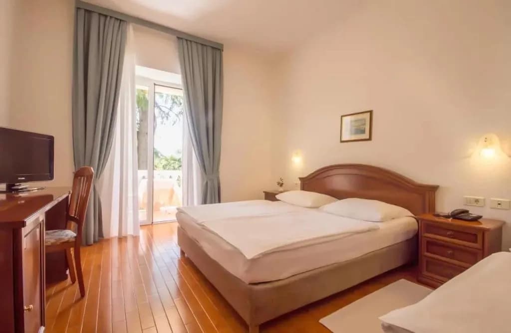 Hotel Marko room with double bed, wooden floors, and balcony access through sheer and blue curtains.