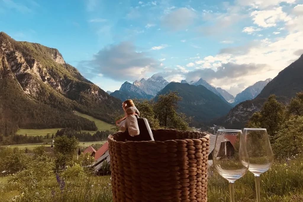 Wine bottle in basket and two empty glasses with view towards Dovje mountains.